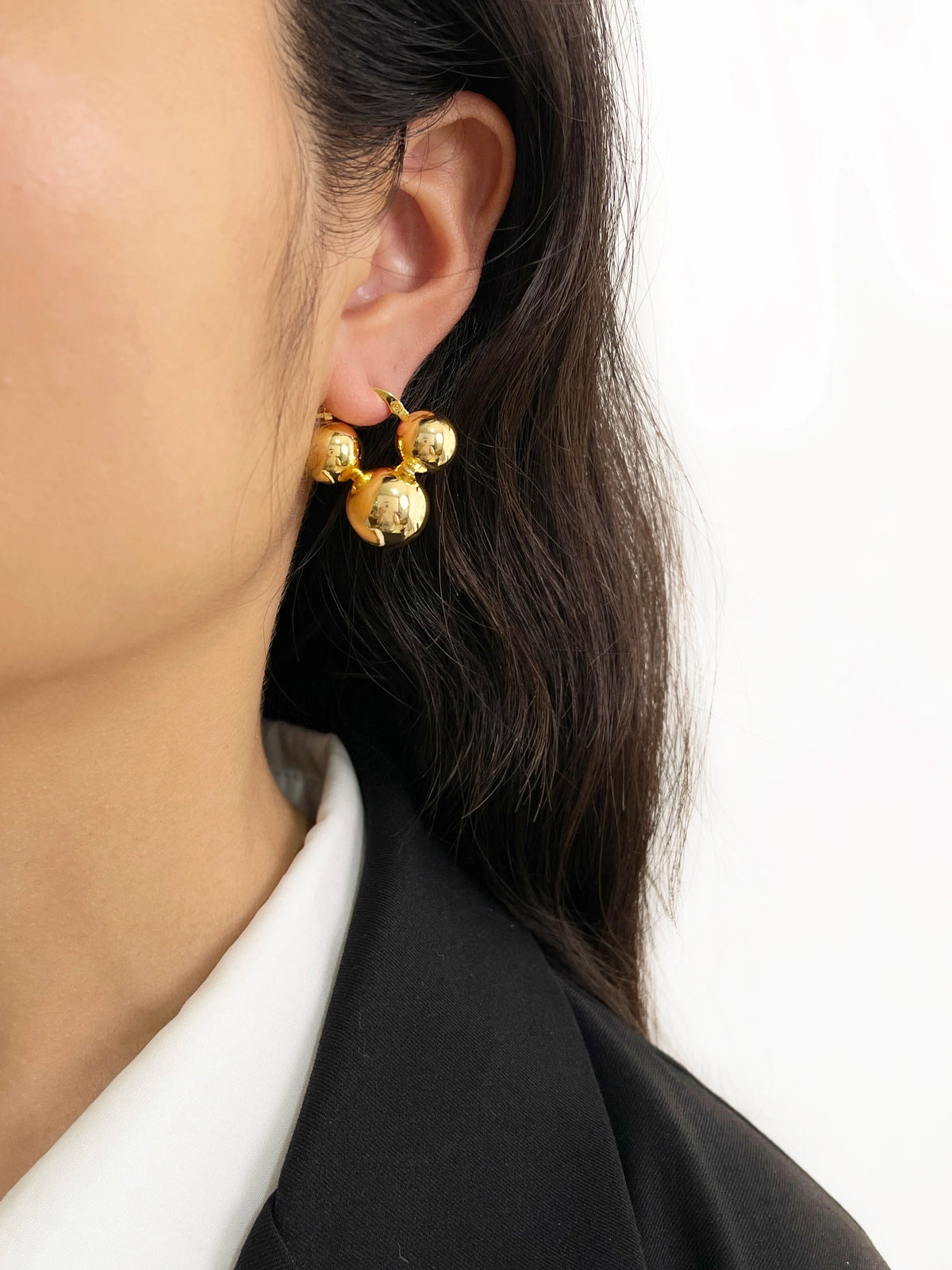 Glossy gold metal hoop earrings with clustered spherical beads, worn on earlobe.