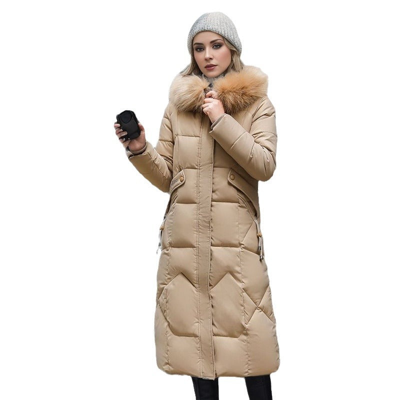 A woman wears a knee-length, quilted beige puffer coat with a large faux fur hood against a white background.