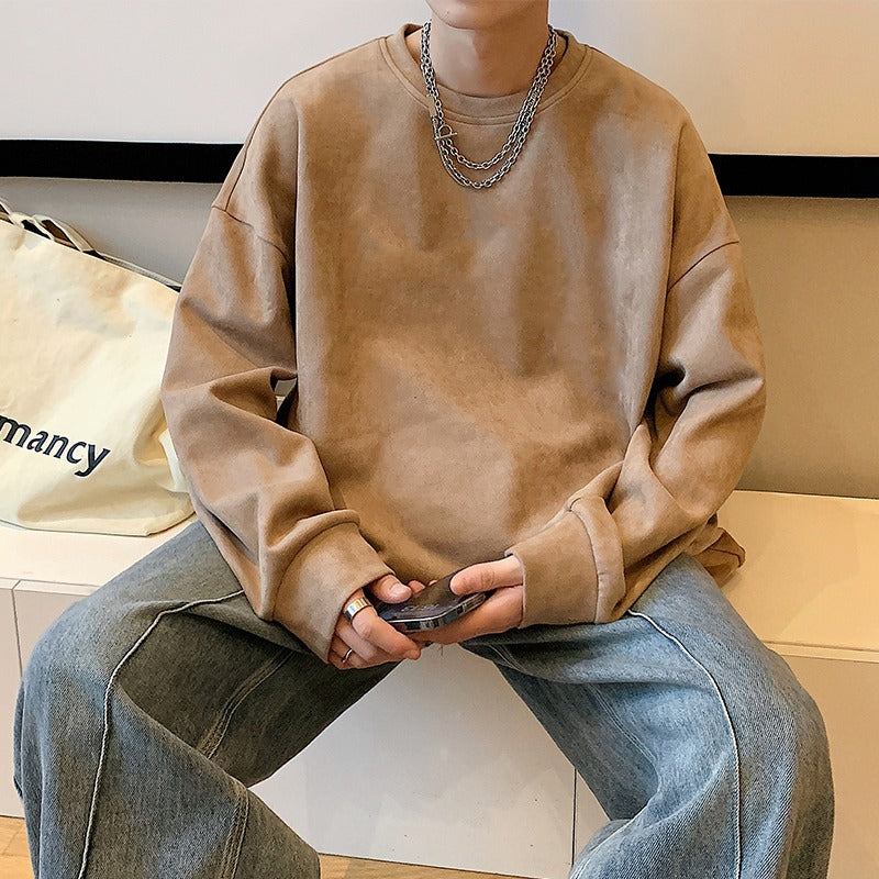A plain brown suede sweatshirt with long sleeves, worn with layered silver chain necklaces and loose blue jeans.