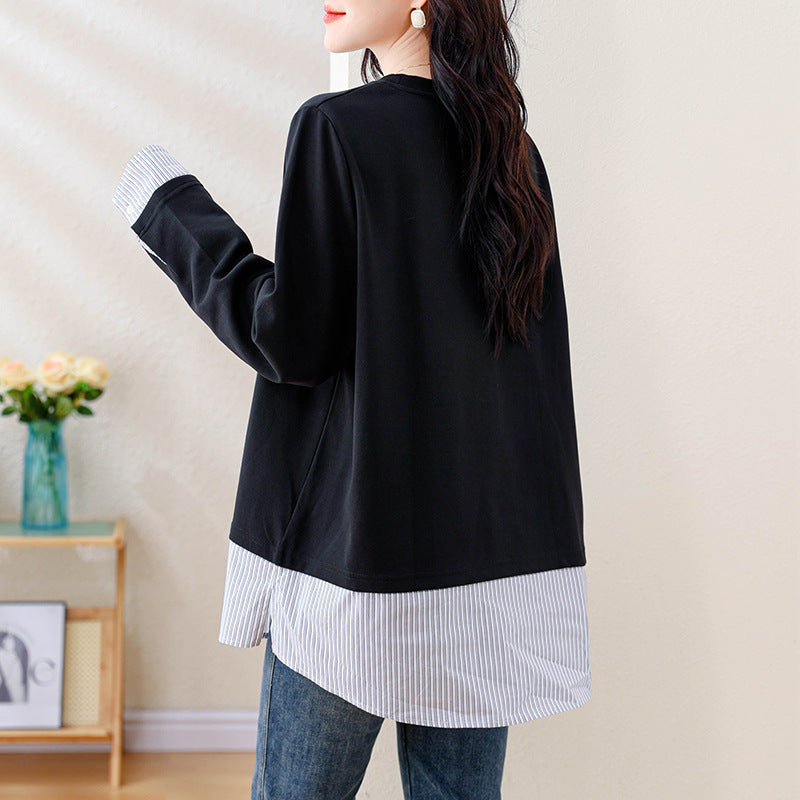 A person wearing a black long-sleeve top with white striped cuffs and a striped hem.