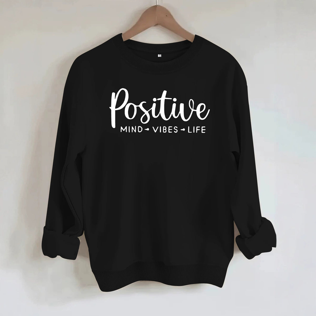 Black crewneck sweatshirt with "Positive MIND VIBES LIFE" text in white on the front, hanging on a hanger.