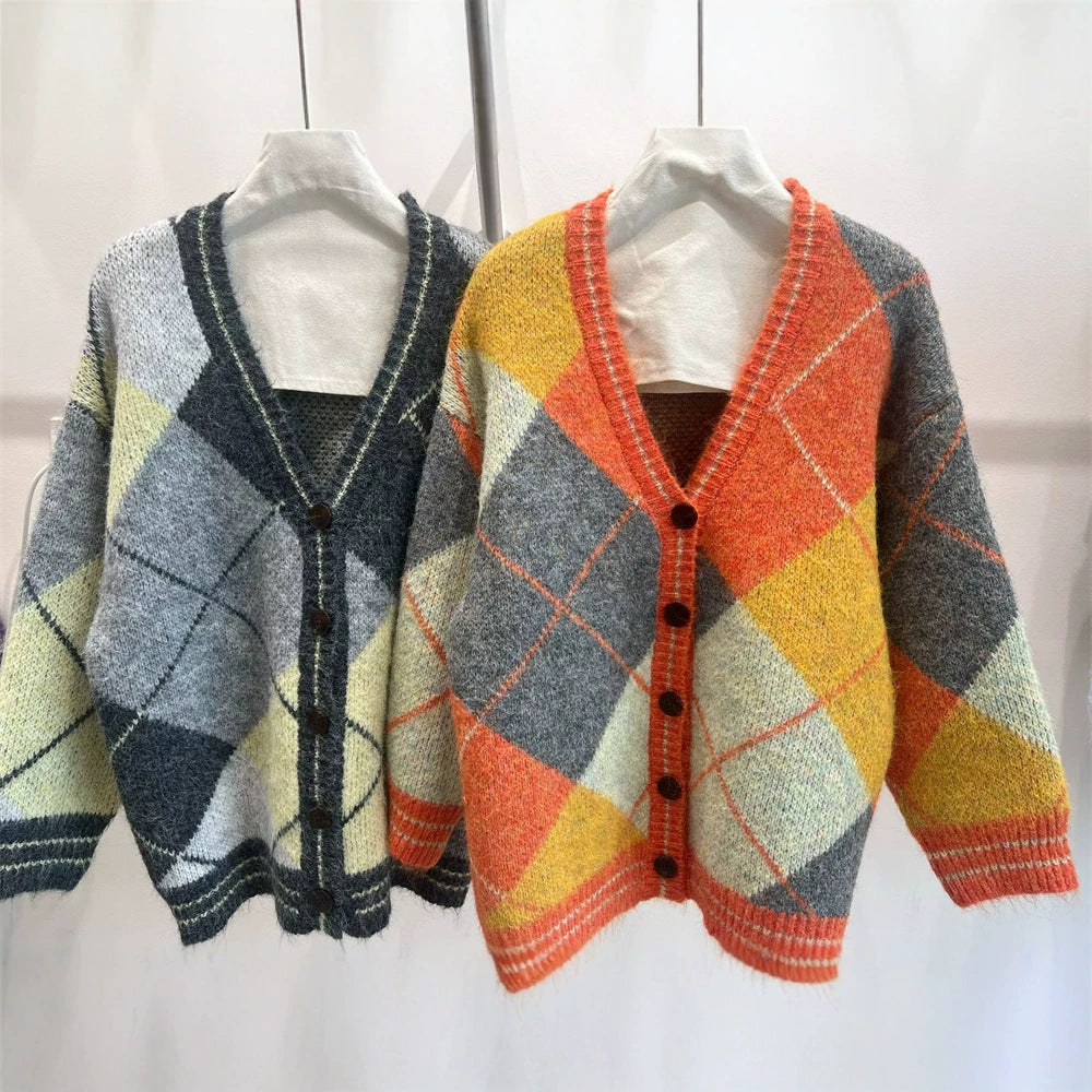 Two color-blocked diamond-patterned V-neck knit cardigans hang on white hangers against a plain wall.
