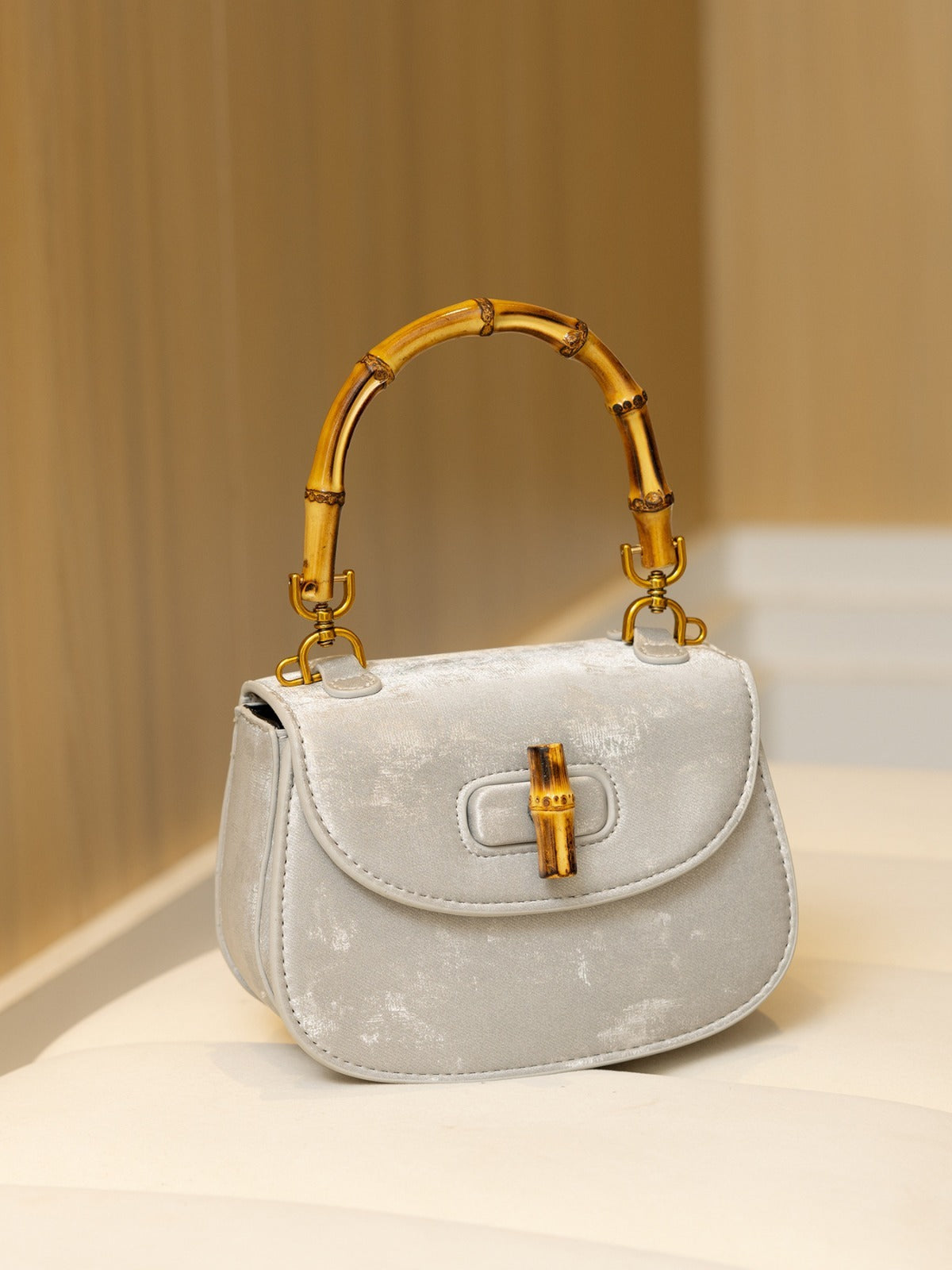 Gray velvet handbag with distressed pattern, curved flap style, and a bamboo handle and turnlock closure.