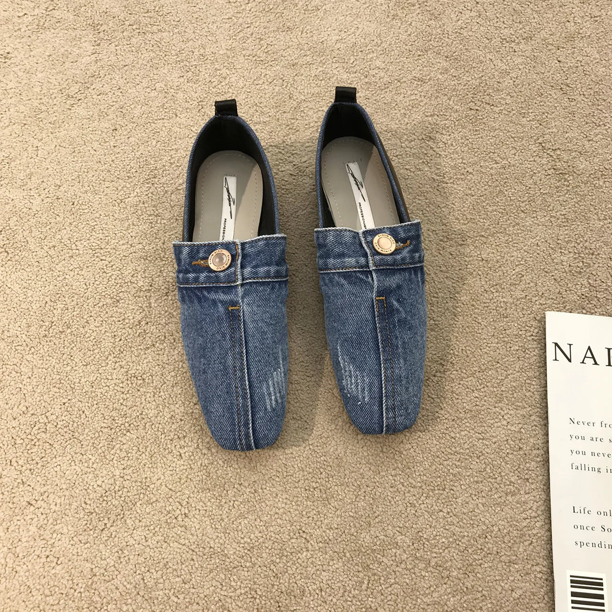 Blue denim slip-on flat shoes with center seams, distressed details, and a buttoned front strap.