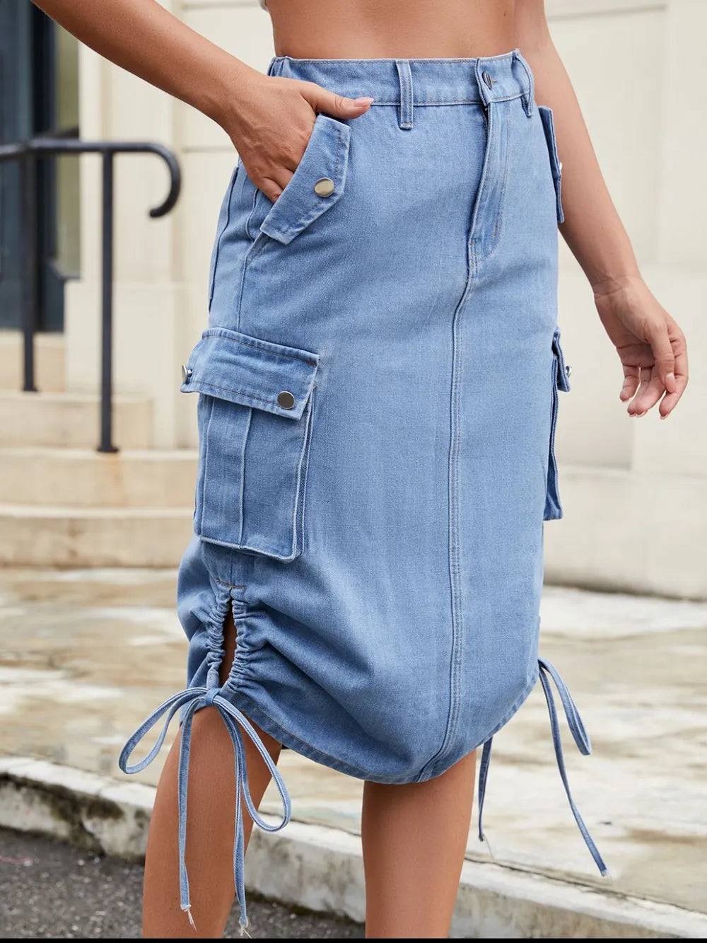 Light blue denim cargo skirt with large flap pockets, button details, and ruched drawstrings at the hem.