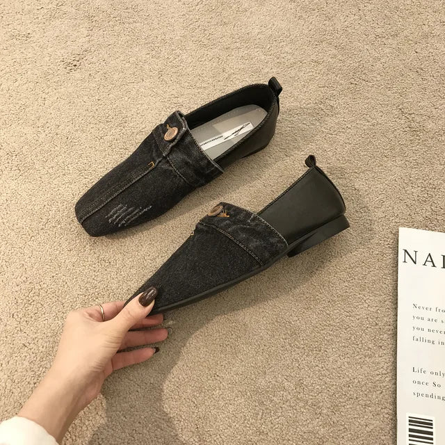 Black denim loafers with pointed toes, decorative buttons, and distressed detailing on the front.