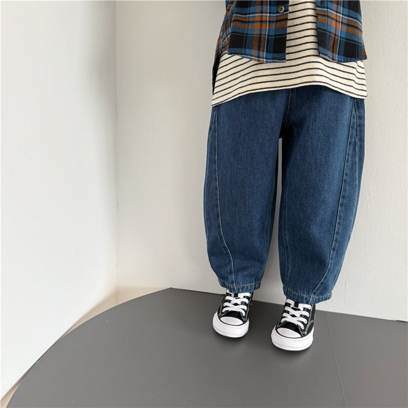 Dark blue denim barrel-leg pants with front seam details, worn with a striped shirt and plaid flannel.