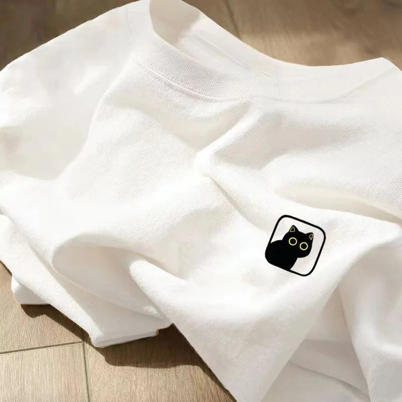 A folded white round-neck t-shirt with a small black cat patch featuring yellow eyes on the chest.