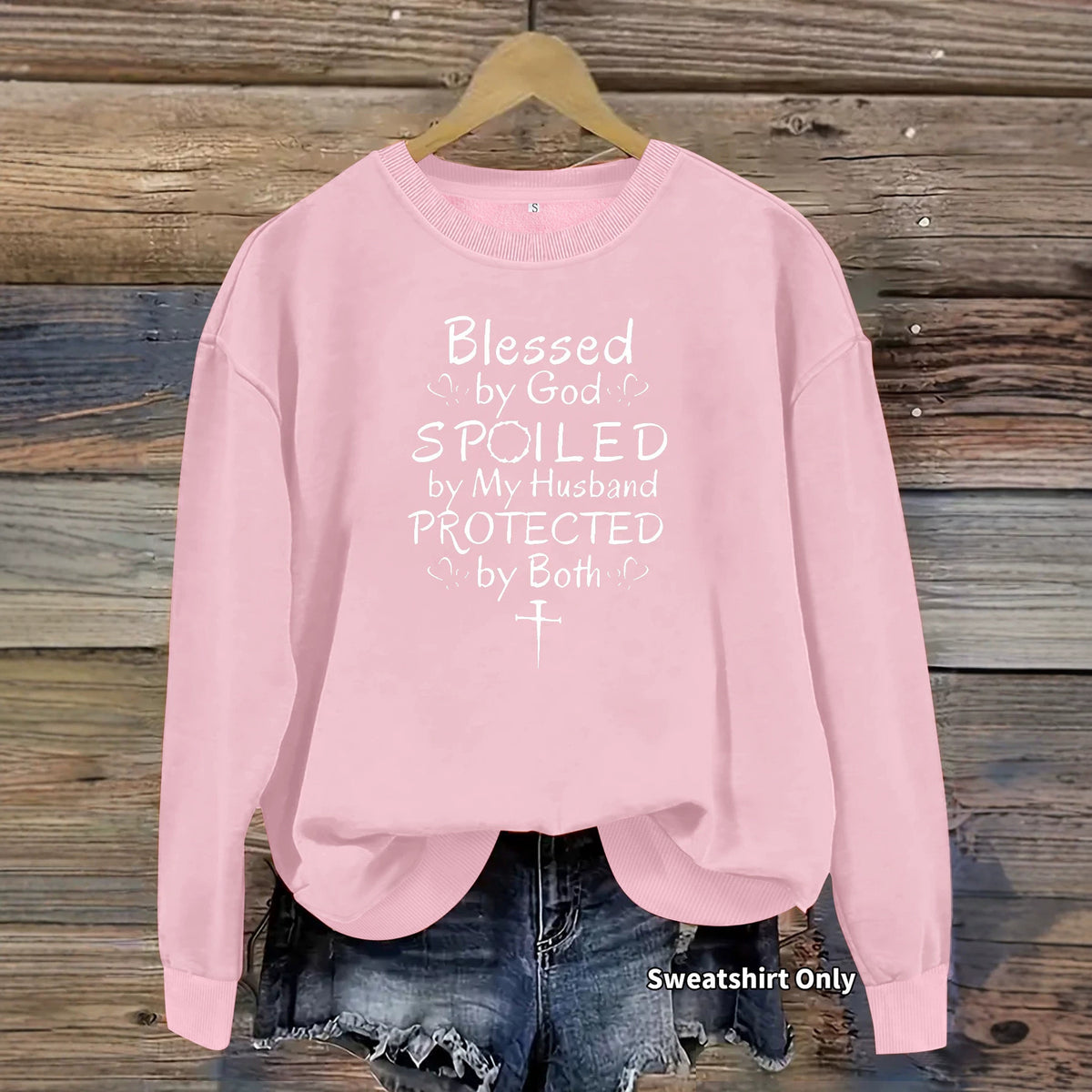 Pink crewneck sweatshirt with white text "Blessed by God SPOILED by My Husband PROTECTED by Both" and a cross.