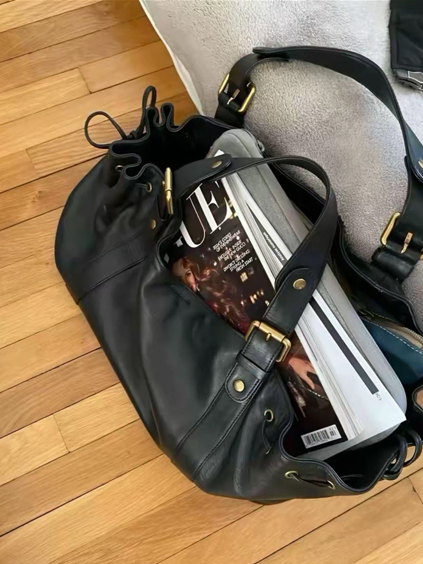 Black leather slouchy shoulder bag with gold-tone hardware, a drawstring closure, and magazines inside.
