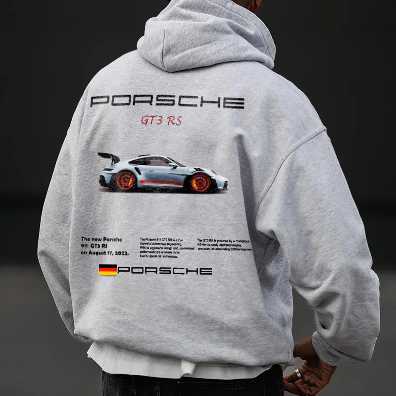 A person wearing a grey pullover hoodie printed with a Porsche graphic and text on the back.