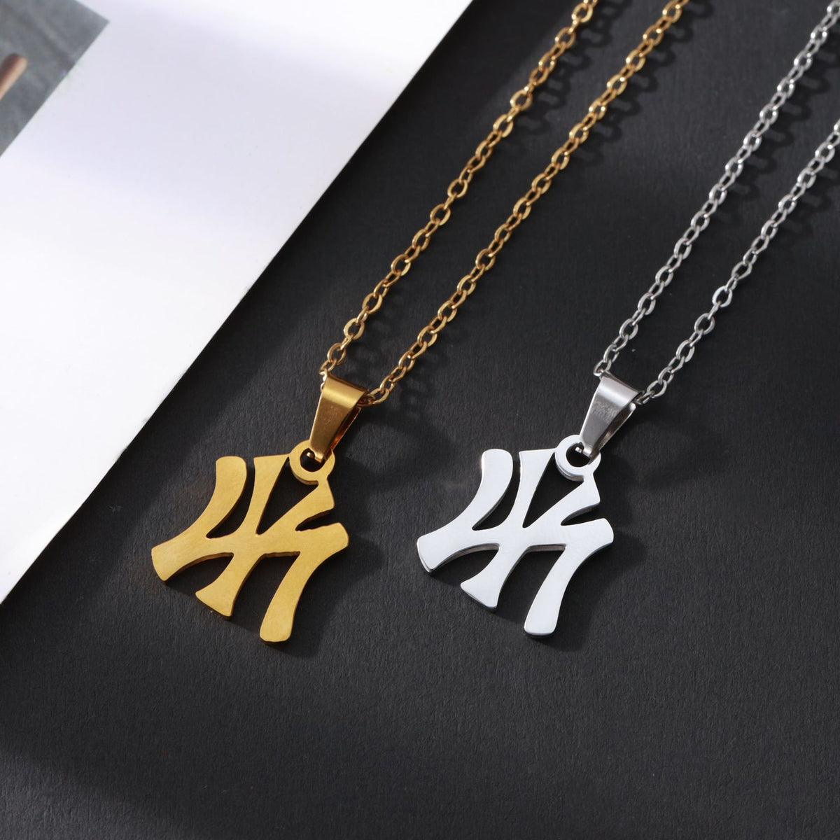 Gold and silver stainless steel chain necklaces with Yankees logo pendants on a black surface.