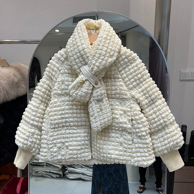 A short, off-white textured puffer jacket with a matching scarf hangs on a rack against a mirror.