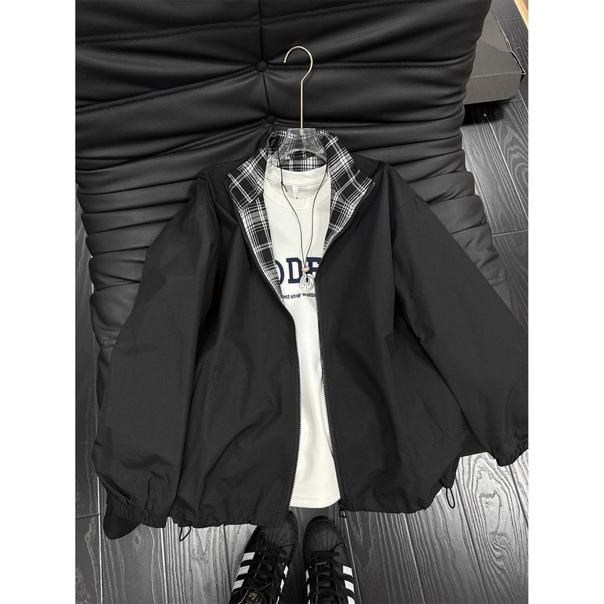 Black zip-up jacket with plaid collar, layered over a white t-shirt on a hanger.