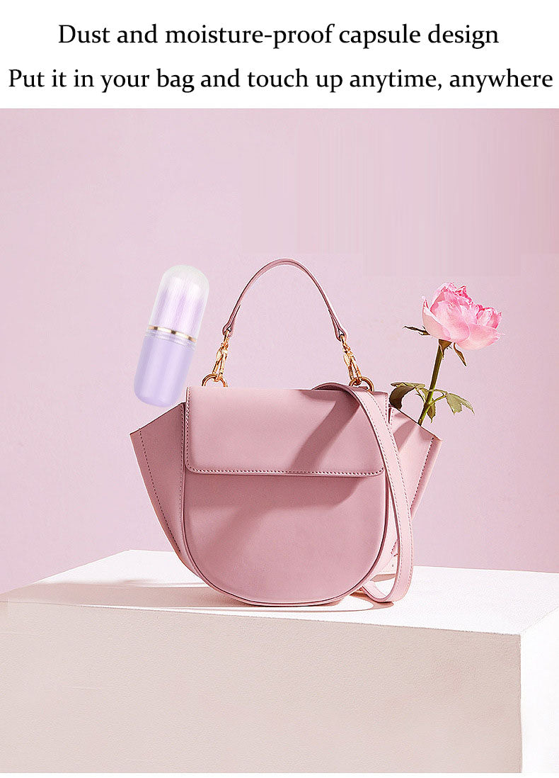 Light purple capsule-shaped makeup brush floating above a pink leather handbag, next to a pink rose on a white surface.