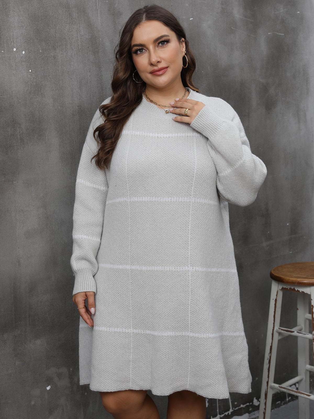 A plus-size model wears a grey knit round-neck long-sleeve sweater dress with a white grid pattern.