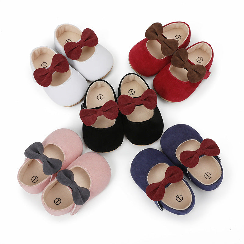 Five pairs of baby Mary Jane shoes in white, red, black, pink, and navy, each with a contrasting bow.