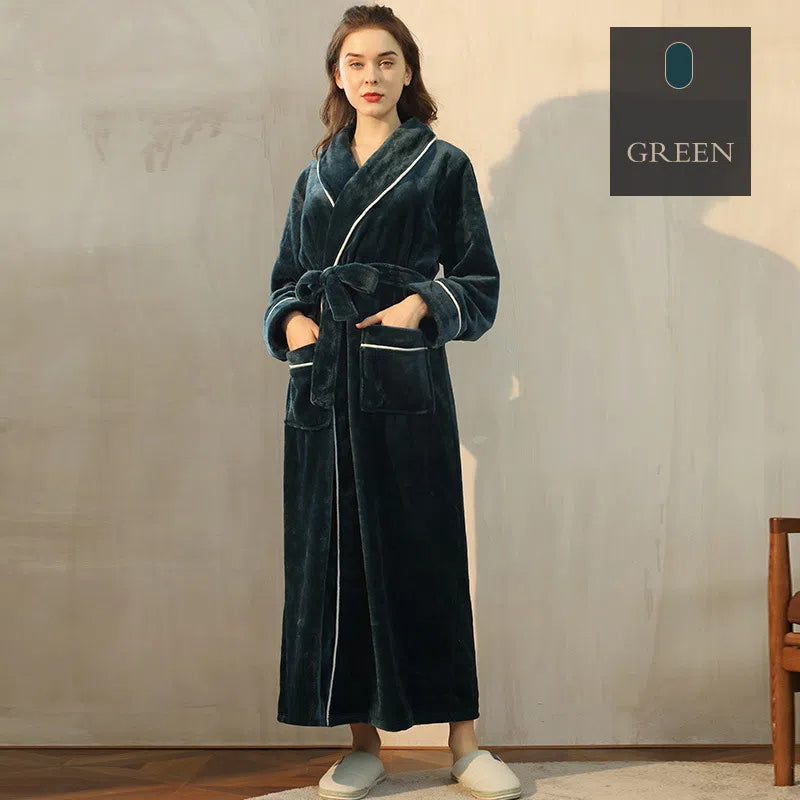 A woman in a long, dark green plush robe with a matching belt, white piping, and front pockets.