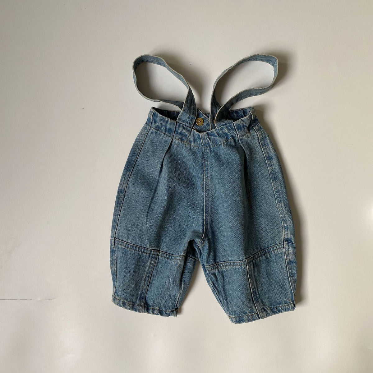 Blue denim toddler overalls with pleated front, elastic waistband, button, and attached shoulder straps.
