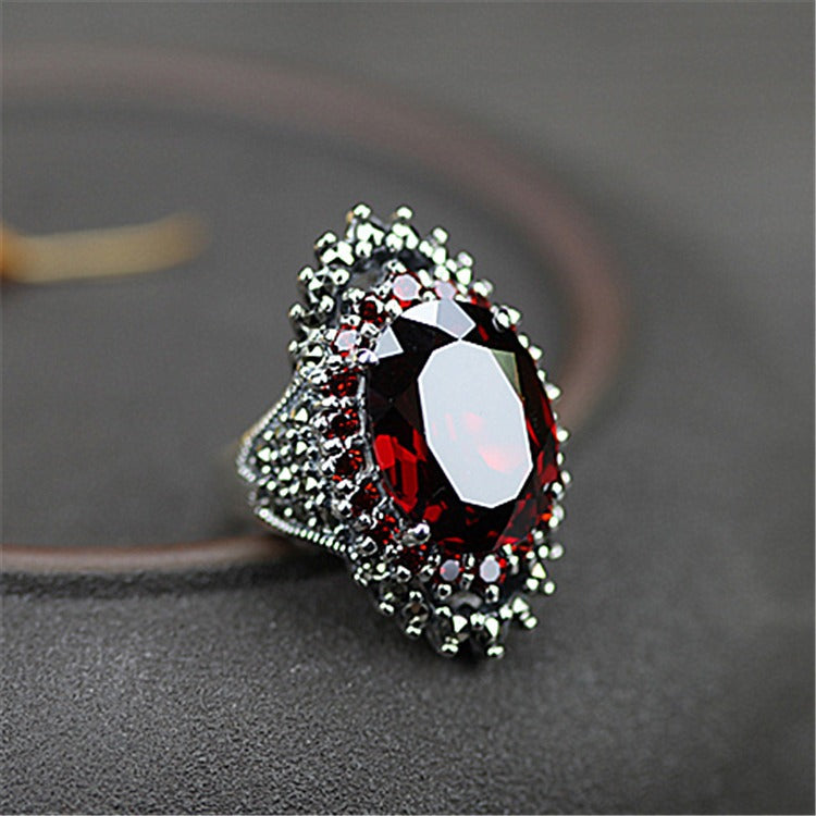 An ornate silver ring features a large oval red gemstone surrounded by smaller red and dark stones.
