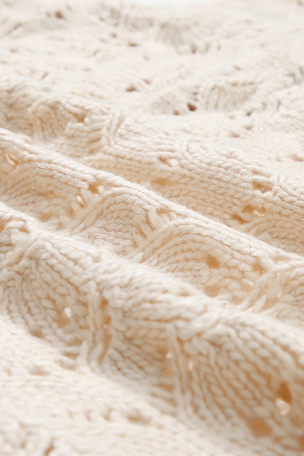 Close-up of beige textured knit fabric with an open cable pattern.