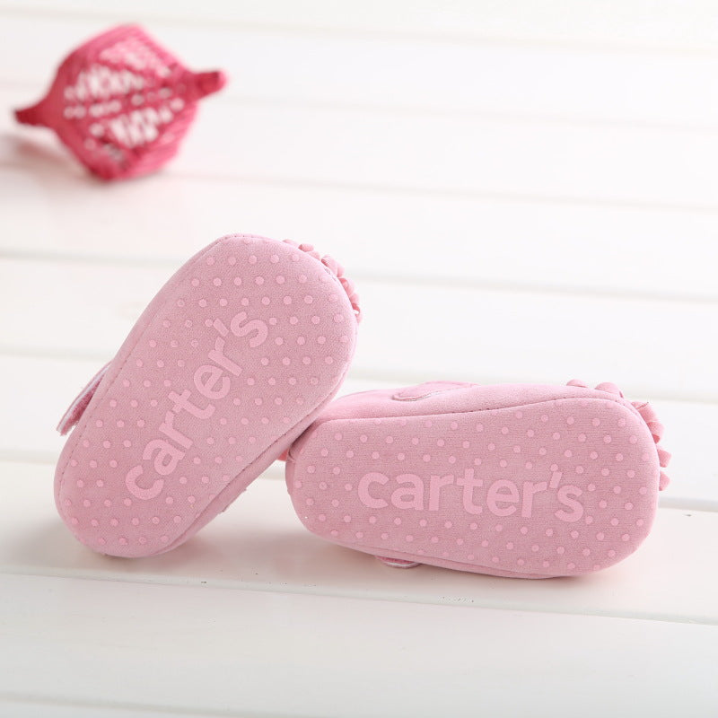 Pink baby shoes with textured soles displaying the brand name carter's and dotted non-slip grips.