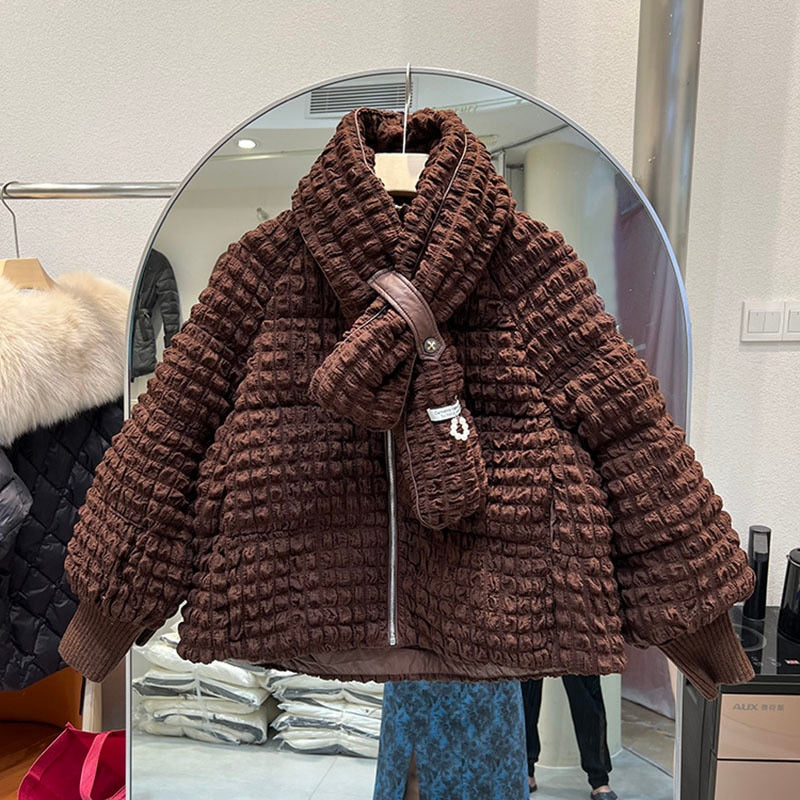 A dark brown puffer jacket with textured pleats, a matching scarf, and ribbed cuffs hangs on a hanger.