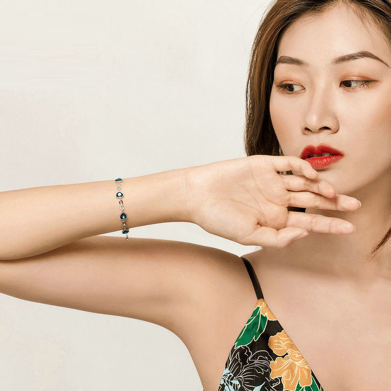 A woman wearing a silver chain bracelet featuring blue heart-shaped charms.
