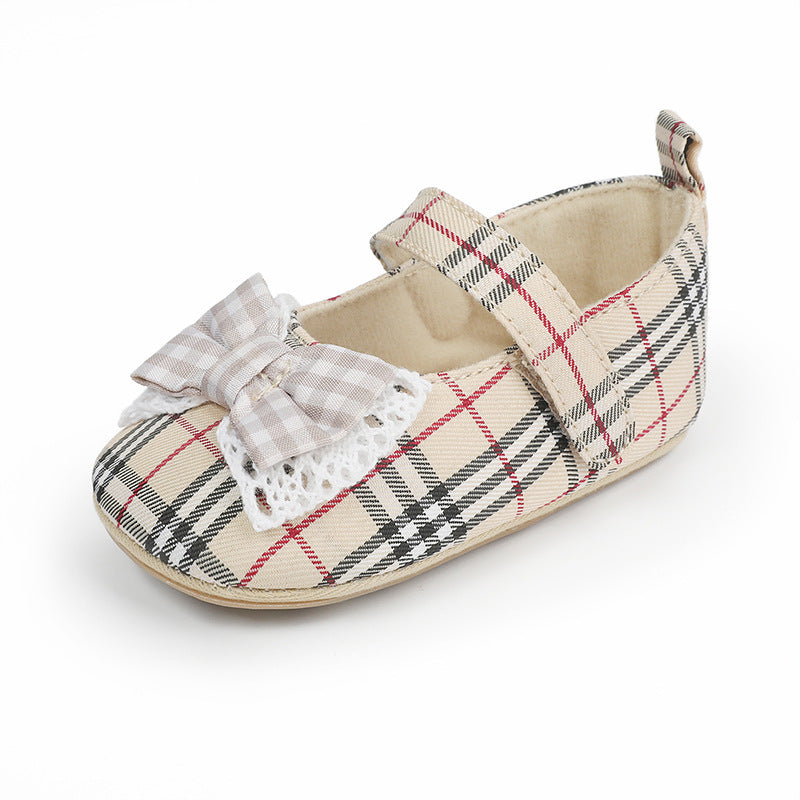 Beige plaid canvas baby shoe with a strap, white lace trim, and a matching bow.