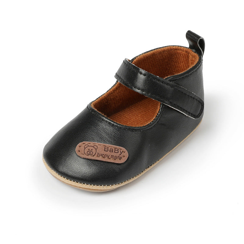Black faux leather baby shoe, Mary Jane style, with brown lining, hook-and-loop strap, and a bear logo patch.