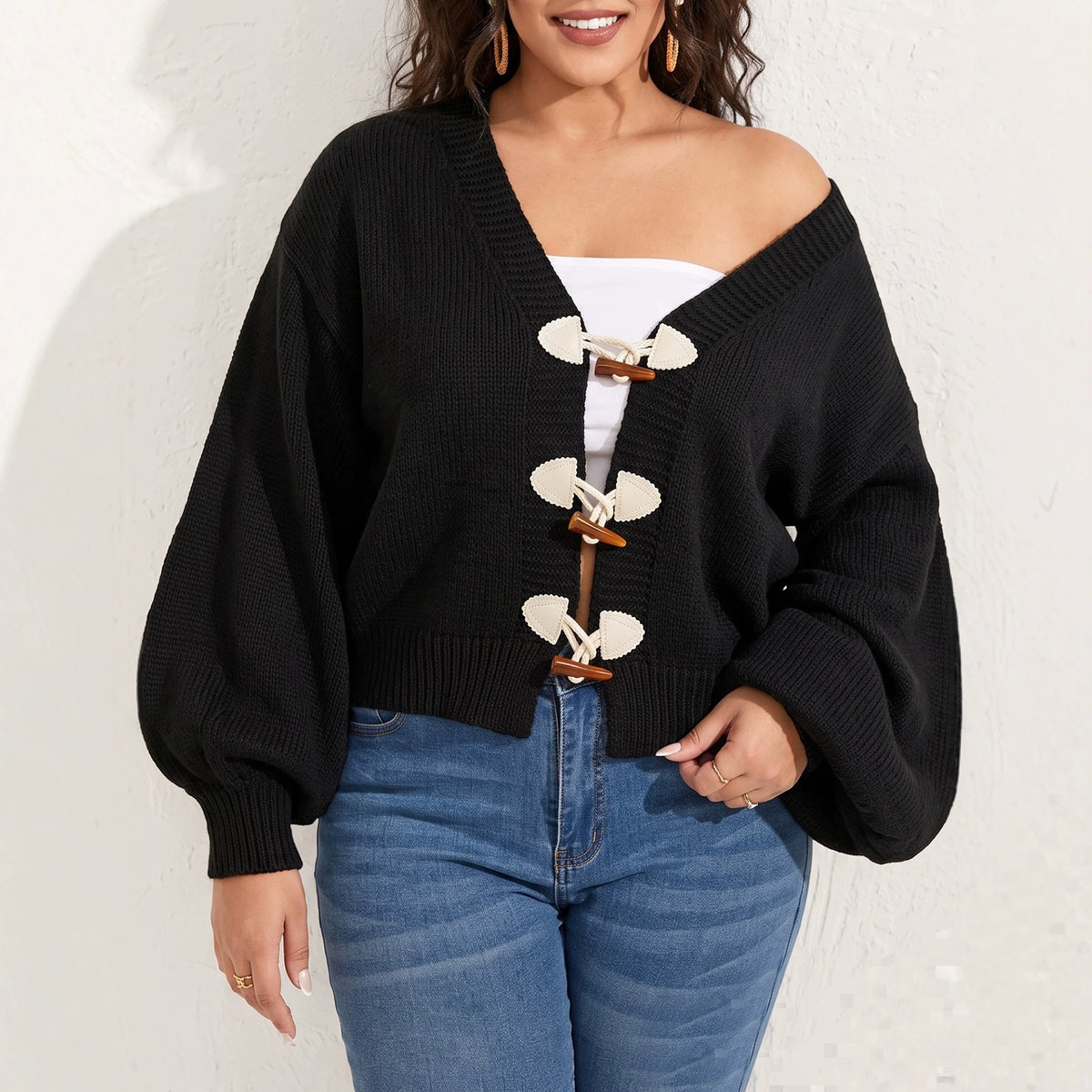 A plus-size woman wearing a black knit cardigan with bishop sleeves and three toggle buttons.