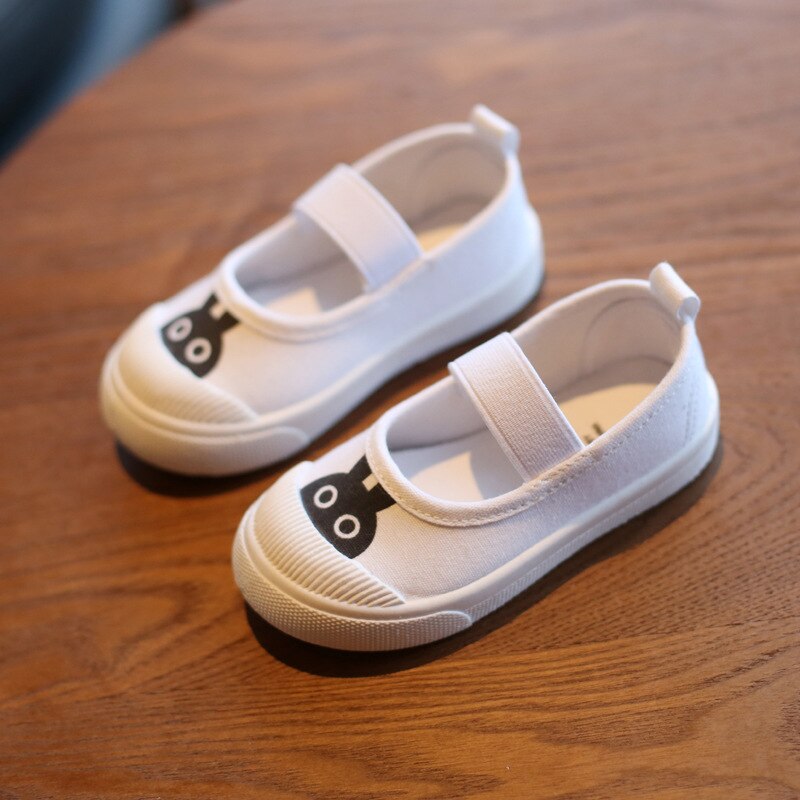 White canvas Mary Jane shoes with black cat face print on toes and elastic strap.