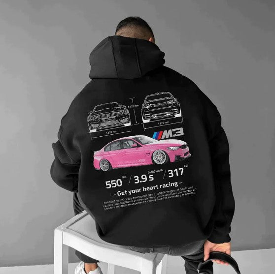 A man wearing a loose black hoodie printed with a pink car graphic and text on the back.