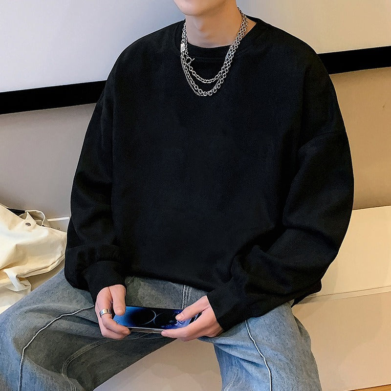A man wears a casual, solid black crewneck sweatshirt in cotton, paired with silver chain necklaces and jeans.