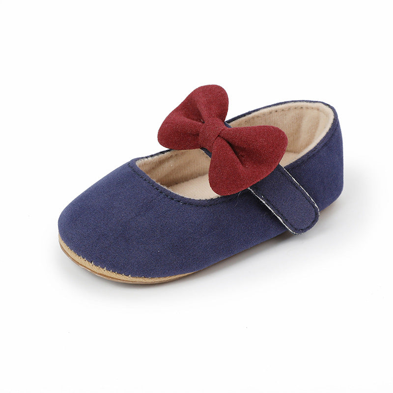 Navy blue baby shoe with a red bow, flat style, fabric material, and velcro strap.