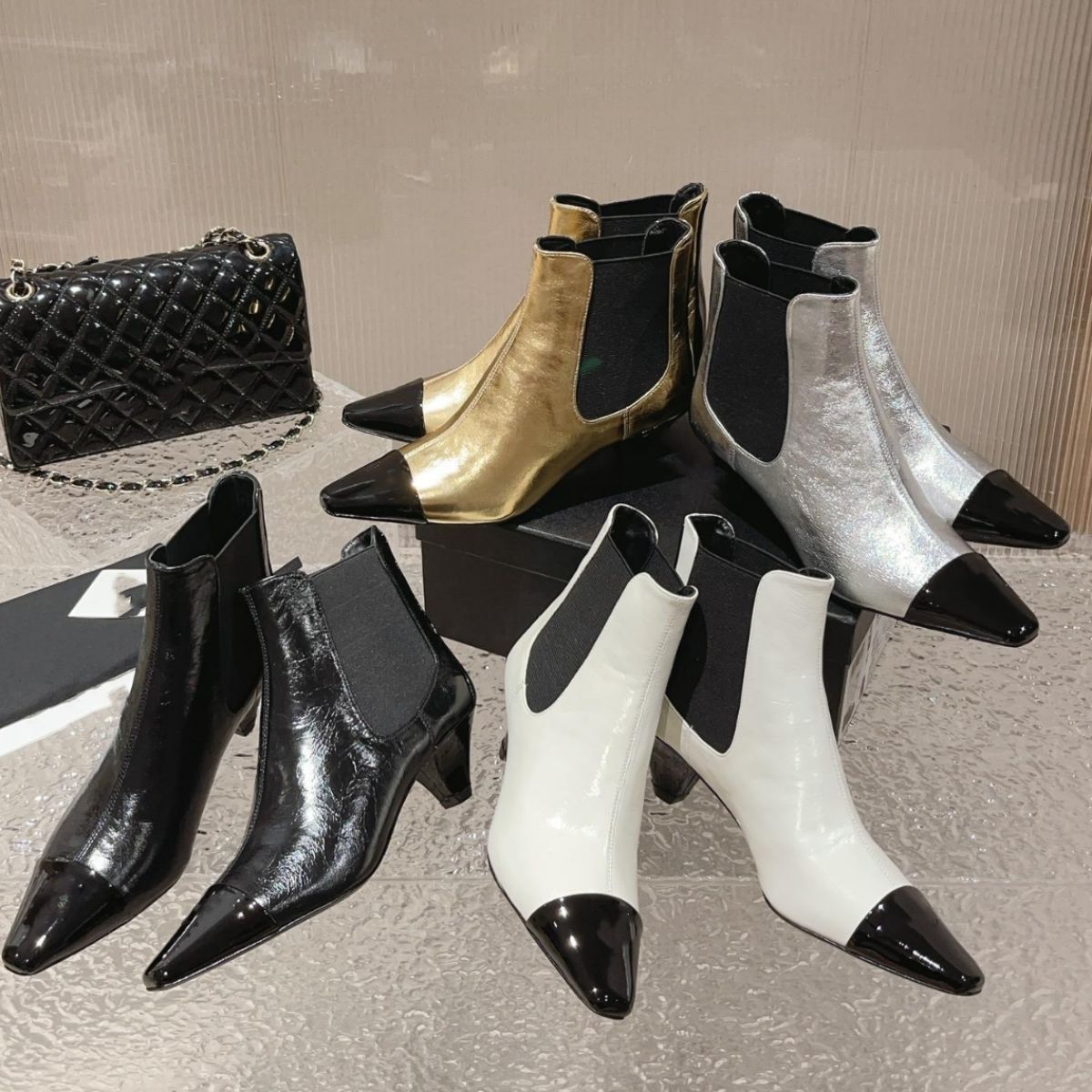 Four pairs of patent leather Chelsea boots in gold, silver, black, and white, with contrasting black toes.