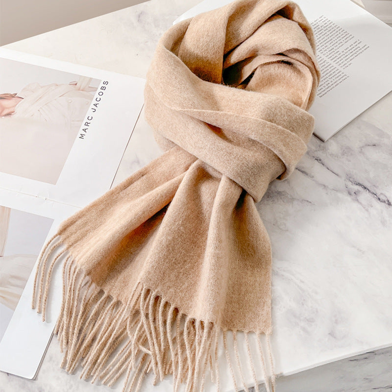 Beige wool winter scarf with fringe ends, styled in a loop on a marble surface.