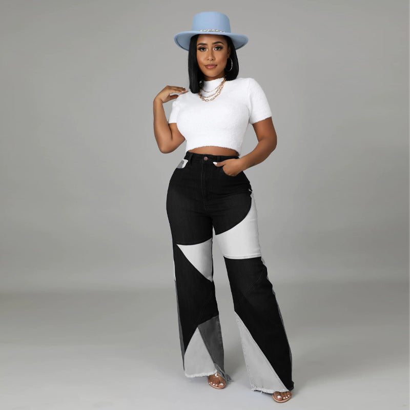A woman wearing a white short-sleeve crop top and color-blocked denim pants with black, grey, and white geometric panels.
