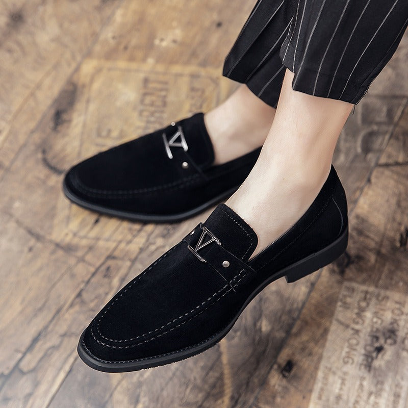 Black suede loafers with a silver V-shaped bit and stitching detail on a wooden floor.