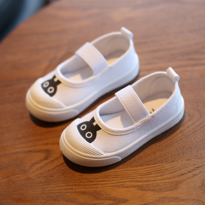 White canvas Mary Jane shoes featuring a black rabbit face on the toe and a secure elastic strap.