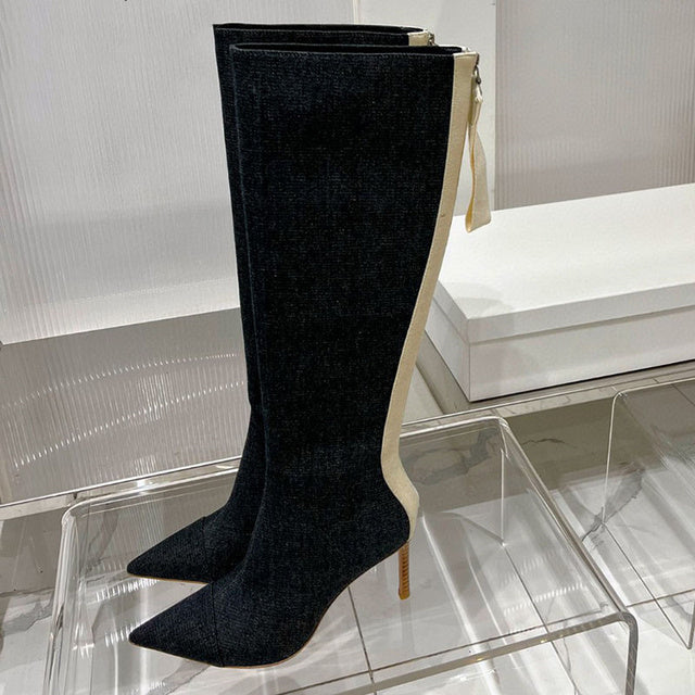 Dark blue denim knee-high boots with stiletto heels, pointed toes, and cream-colored back panels with zippers.
