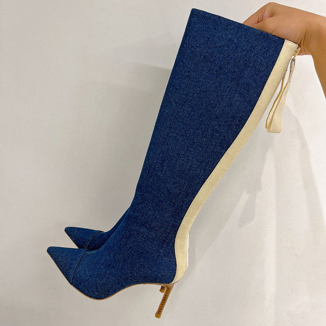 Knee-high dark blue denim boots with a pointed toe, stiletto heel, and cream zipper back trim.