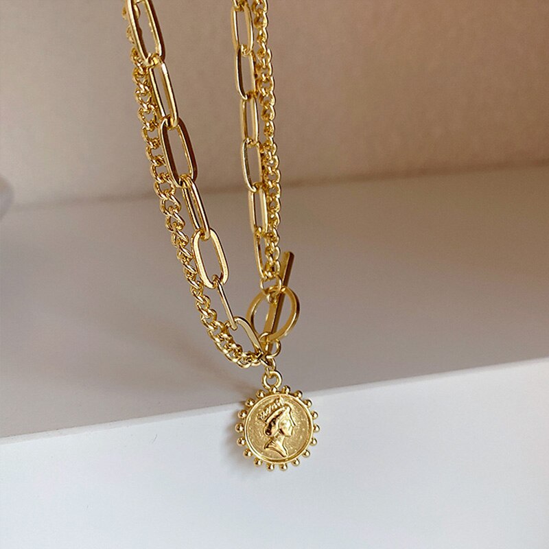 Gold-tone metal layered necklace with a coin pendant featuring a profile portrait and a toggle clasp.