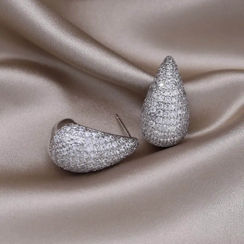 Two pavé-set teardrop earrings rest on a shiny grey silk background.