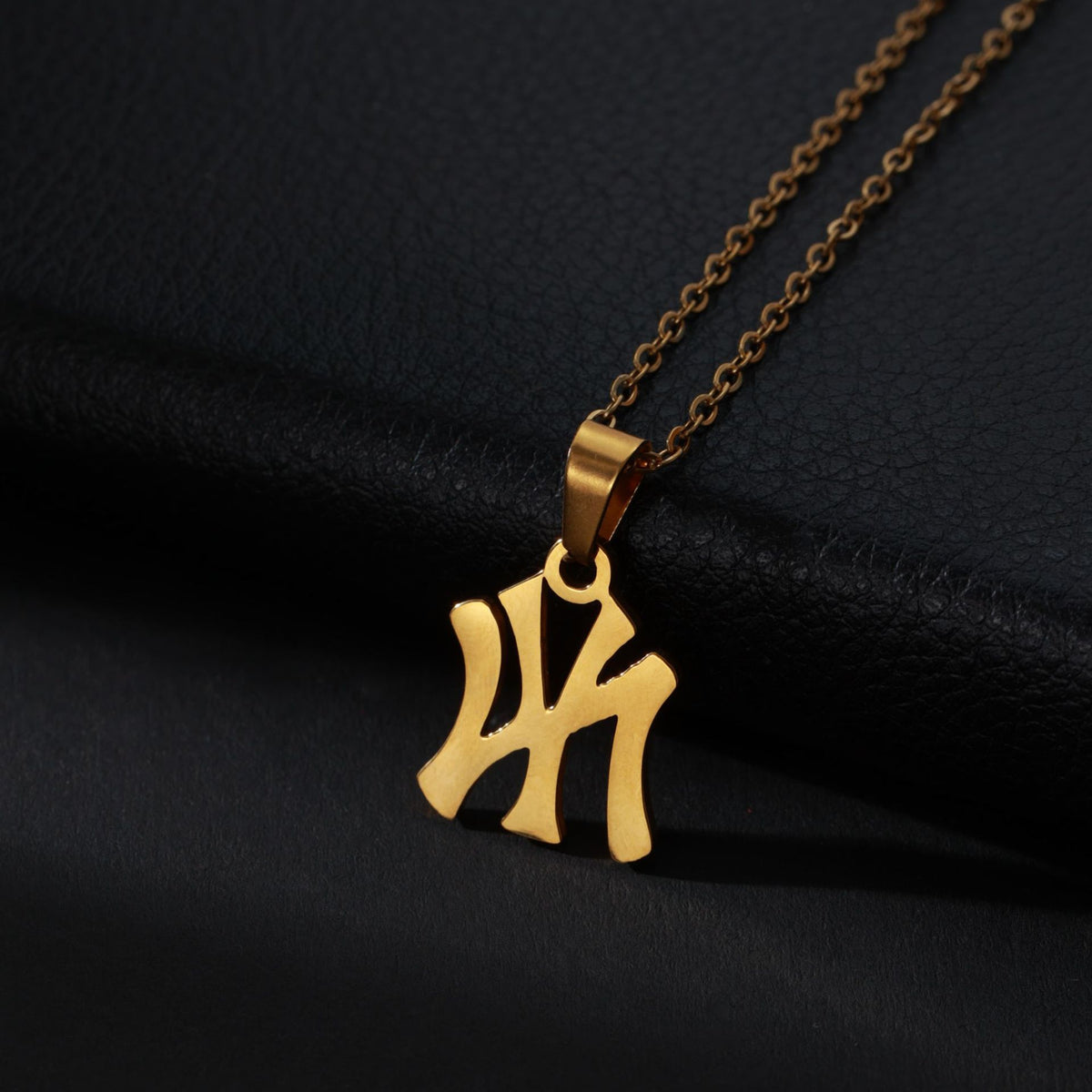 Gold metal NY Yankees logo pendant necklace on a chain against a black background.
