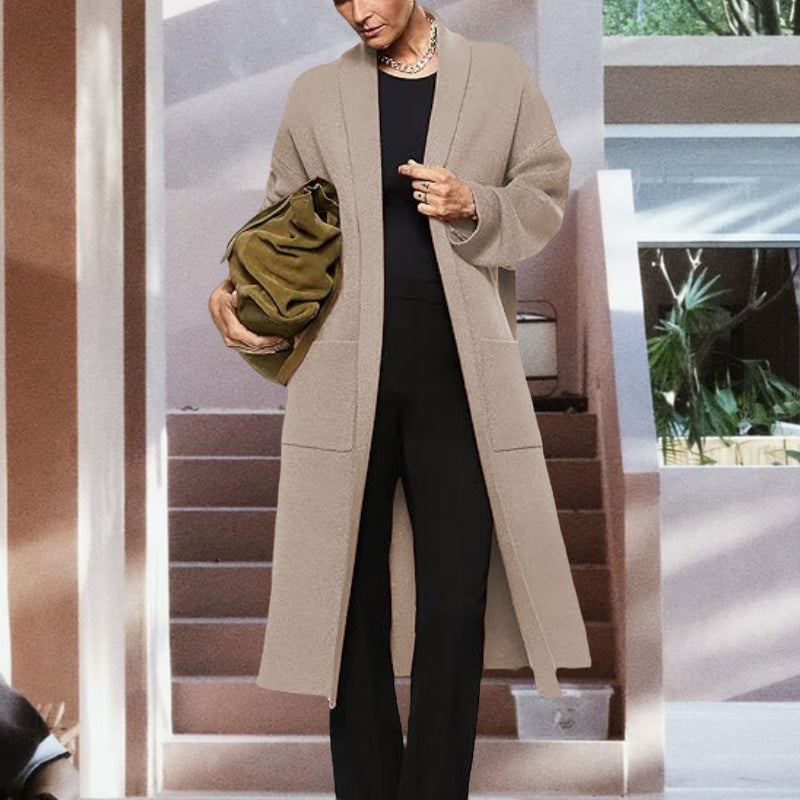 Beige open-front knit cardigan with long sleeves, shawl collar, and patch pockets over black pants.