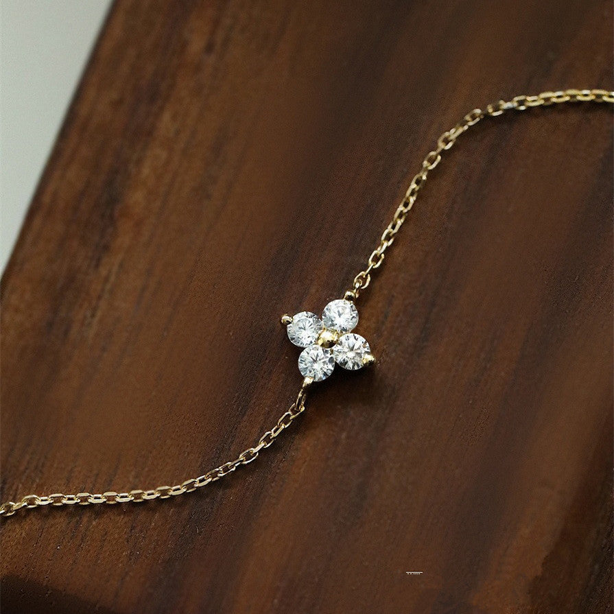 Gold metal chain bracelet featuring a four-petal flower charm made of four sparkling cubic zirconia stones.