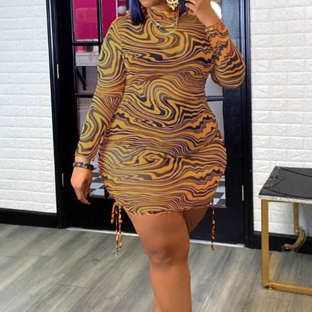 A person wears a long-sleeve yellow mesh dress featuring an abstract black zebra print and side drawstrings.