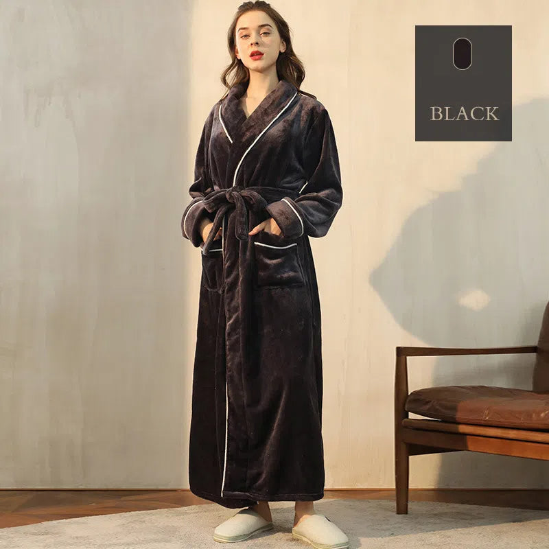 Woman wearing a long black plush robe with white piping, pockets, and a matching tie belt.