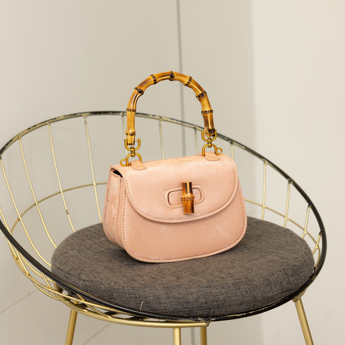 Light pink suede handbag with bamboo handle, gold hardware, and bamboo turn-lock closure sitting on a chair.